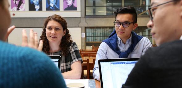 Group of students sitting at a desk having a discussion with laptops